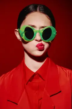 Азиатская девушка в зелёных очках и красном пиджаке на красном фоне