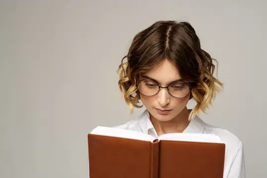 Молодая женщина с волнистыми волосами в очках читает книгу