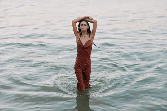 Молодая женщина в шелковом платье стоит по колено в воде