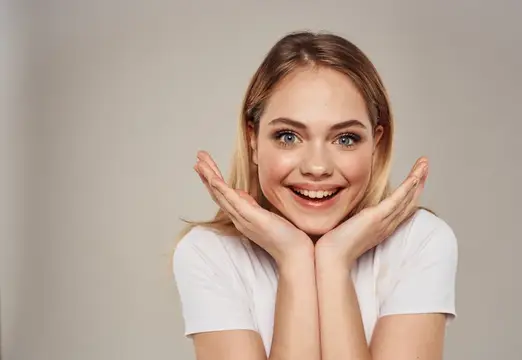 Светловолосая девушка улыбается и подпирает лицо ладонями
