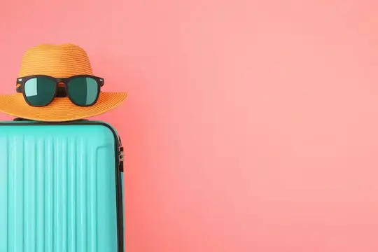 Яркий бирюзовый чемодан с оранжевой шляпой и солнцезащитными очками на розовом фоне вызывает чувства летнего путешествия, приключений и готовности к отпуску
