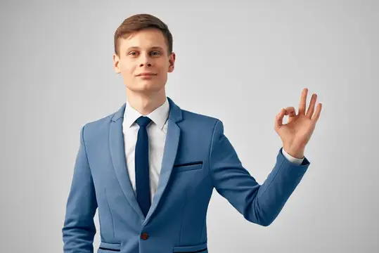Молодой мужчина в синем костюме показывает жест ОК