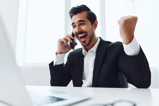 Радостный темноволосый мужчина в костюме празднует успех с телефоном