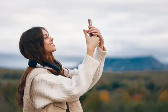 Улыбающаяся девушка фотографирует на телефон горный пейзаж