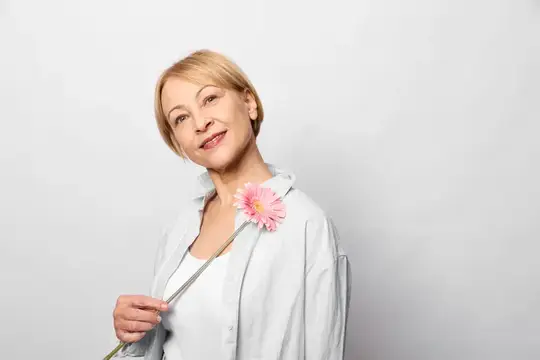 Светловолосая женщина с розовым цветком в руке на сером фоне