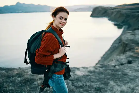 Женщина-туристка на закате у моря в горах с рюкзаком за спиной