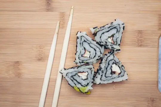 Кусочки роллов с лососем и палочки на бамбуковой доске