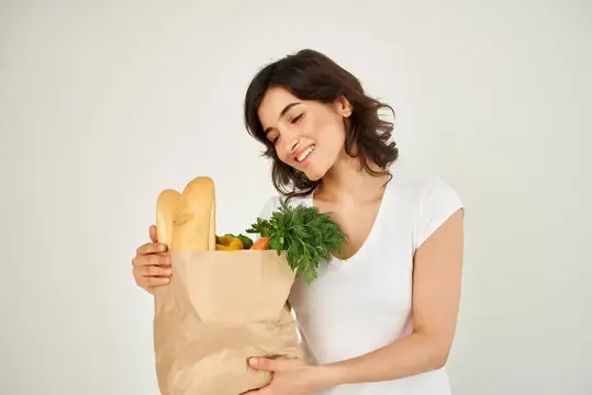 Улыбающаяся брюнетка с бумажным пакетом продуктов