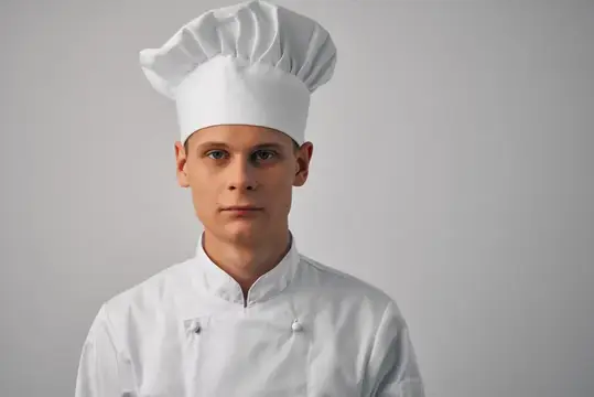 Молодой повар в белом колпаке на сером фоне