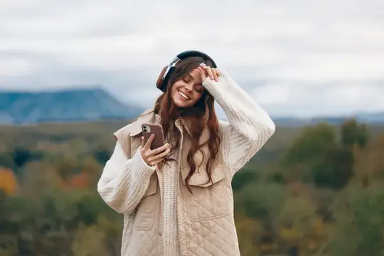 Улыбающаяся девушка в наушниках со смартфоном на фоне осенних гор