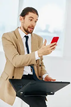 Удивлённый мужчина в бежевом пиджаке смотрит на красный смартфон