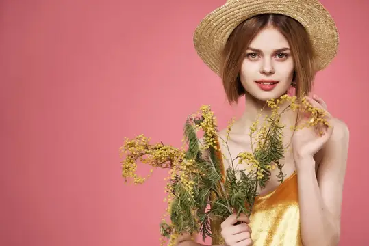 Молодая женщина в соломенной шляпе с ветками мимозы на розовом фоне
