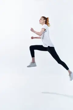 Молодая женщина в спортивной одежде прыгает в высоту на белом фоне