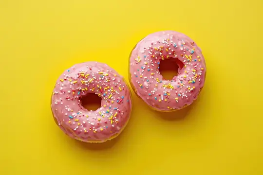 Два пончика с розовой глазурью и посыпкой на жёлтом фоне