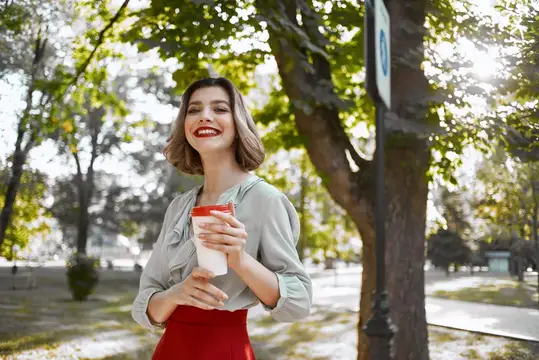 Женщина на улице с чашкой кофе идет по улице