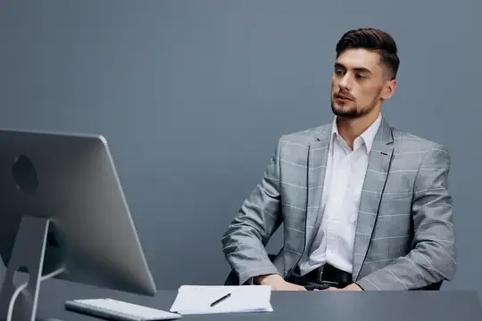 Молодой мужчина в сером пиджаке работает за компьютером в офисе