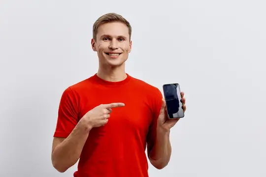 Улыбающийся парень в красной футболке указывает на смартфон