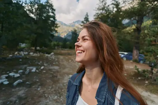Улыбающаяся девушка с длинными волосами на фоне горного леса
