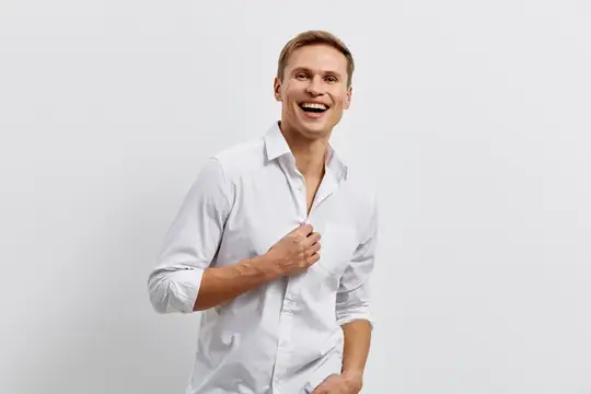 Смеющийся светловолосый мужчина в белой рубашке на сером фоне