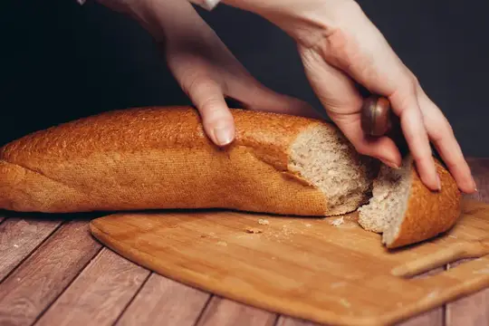 Свежий нарезанный батон на жёлтой салфетке, стоящей на деревянном столе