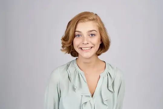 Рыжеволосая девушка искренне улыбается на сером фоне