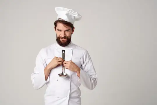 Бородатый повар в белом колпаке держит кухонный пестик