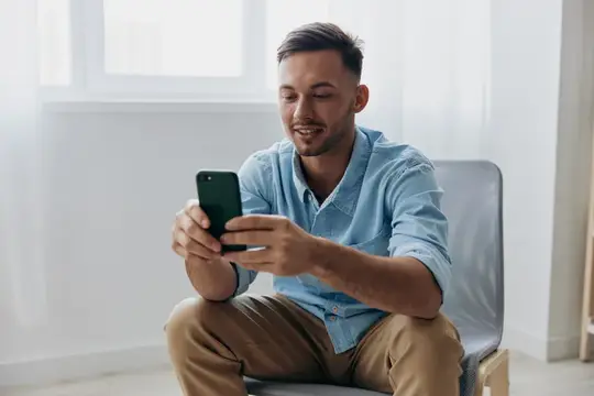 Улыбающийся мужчина в голубой рубашке смотрит в смартфон