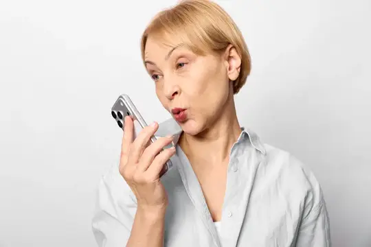 Светловолосая женщина держит смартфон возле лица, разговаривает с удивлением