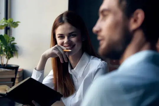 Улыбчивая девушка с карандашом смотрит на коллегу в офисе