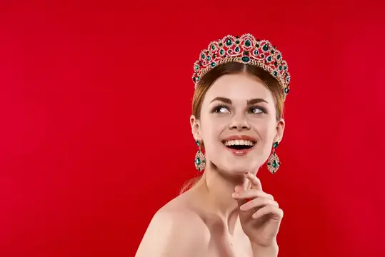 Улыбающаяся девушка в короне с изумрудами на красном фоне
