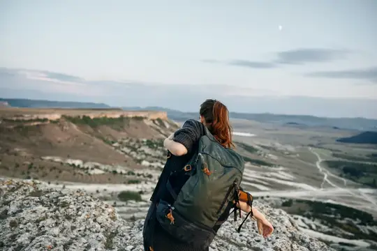 Рыжеволосая путешественница с рюкзаком смотрит на долину с обрыва