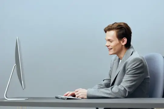 Улыбающийся мужчина в сером пиджаке работает за компьютером