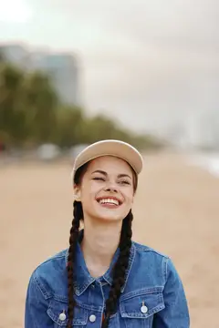 Улыбающаяся девушка с косичками в кепке на пляже