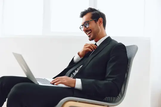 Улыбающийся мужчина в очках и костюме работает за ноутбуком в светлом офисе