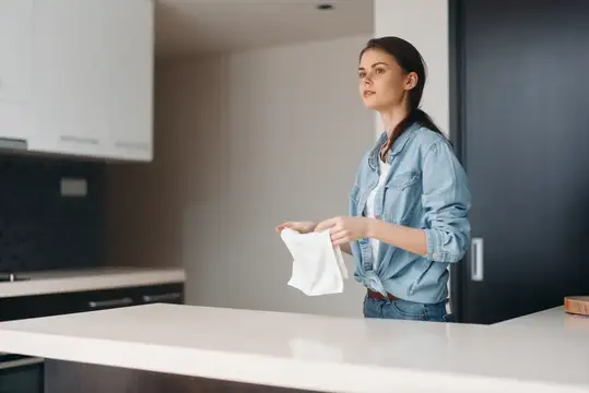 Молодая женщина в джинсовой куртке вытирает стол на светлой кухне