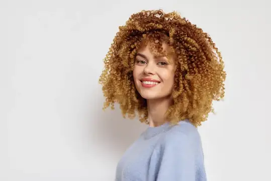 Улыбающаяся девушка с пышными рыжими кудрями на светлом фоне
