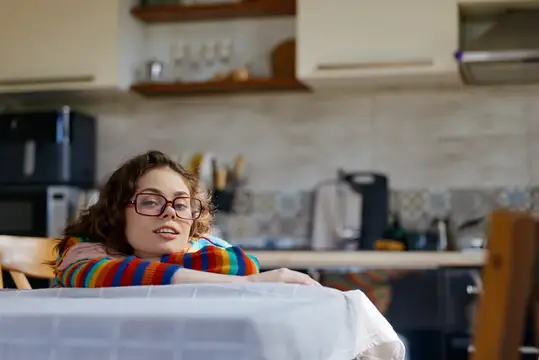 Непринужденная сцена женщины дома на кухне, расслабленная поза, мягкие естественные тона, интимное настроение, повседневная рутина, атмосфера заботы о себе, приглашающая и жизнерадостная атмосфера