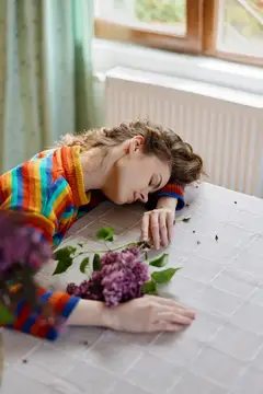 Уставшая девушка лежит на столе с ветками сирени