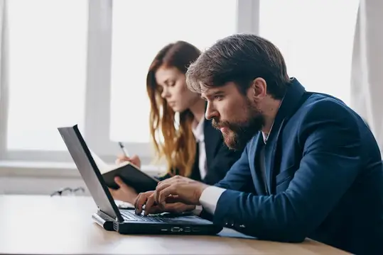 Бородатый мужчина в костюме работает за ноутбуком в офисе