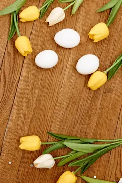 Жёлтые тюльпаны и белые яйца на деревянном столе