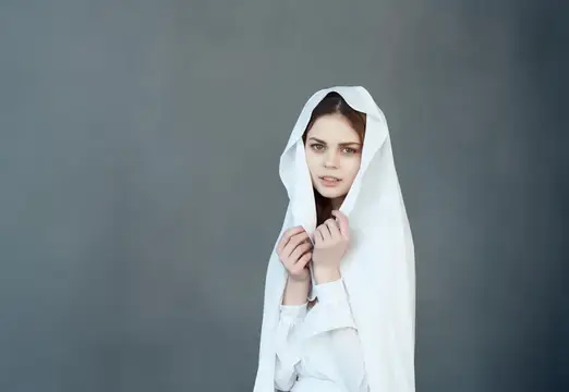 Молодая женщина в белом капюшоне на сером фоне