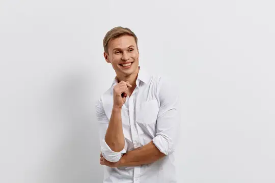 Улыбающийся блондин в белой рубашке смотрит в сторону на сером фоне