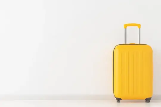Желтый чемодан на колесах стоит у белой стены
