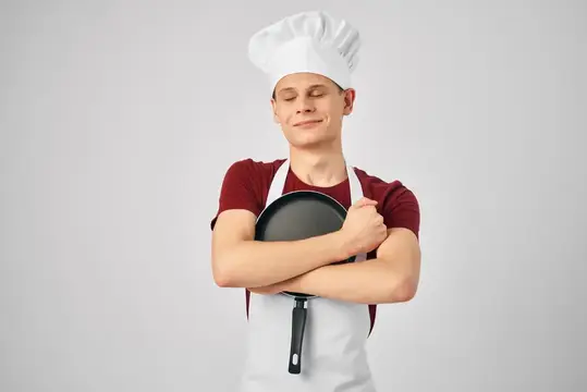 Повар в униформе держит сковороду в руках на профессиональной кухне ресторана