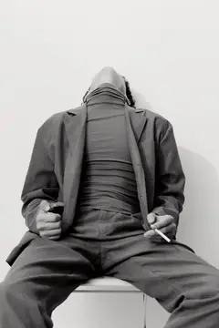 Уставший темнокожий мужчина в костюме откинулся на стуле с сигаретой