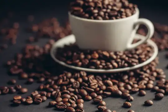 Белая чашка с кофейными зёрнами на тёмном столе