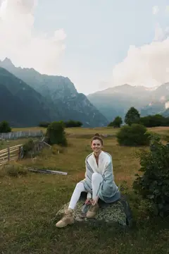 Улыбающаяся девушка сидит на камне на фоне гор