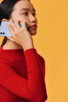 Женщина в красной рубашке с длинным рукавом разговаривает по смартфону на фоне оранжевой стены с сосредоточенным взглядом
