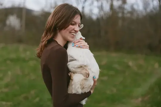 Улыбающаяся женщина в сельской местности держит на руках козлёнка