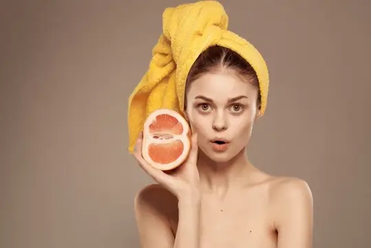 Привлекательная женщина с обнажёнными плечами, ухаживающая за кожей, держит в руке грейпфрут, кадр обрезан